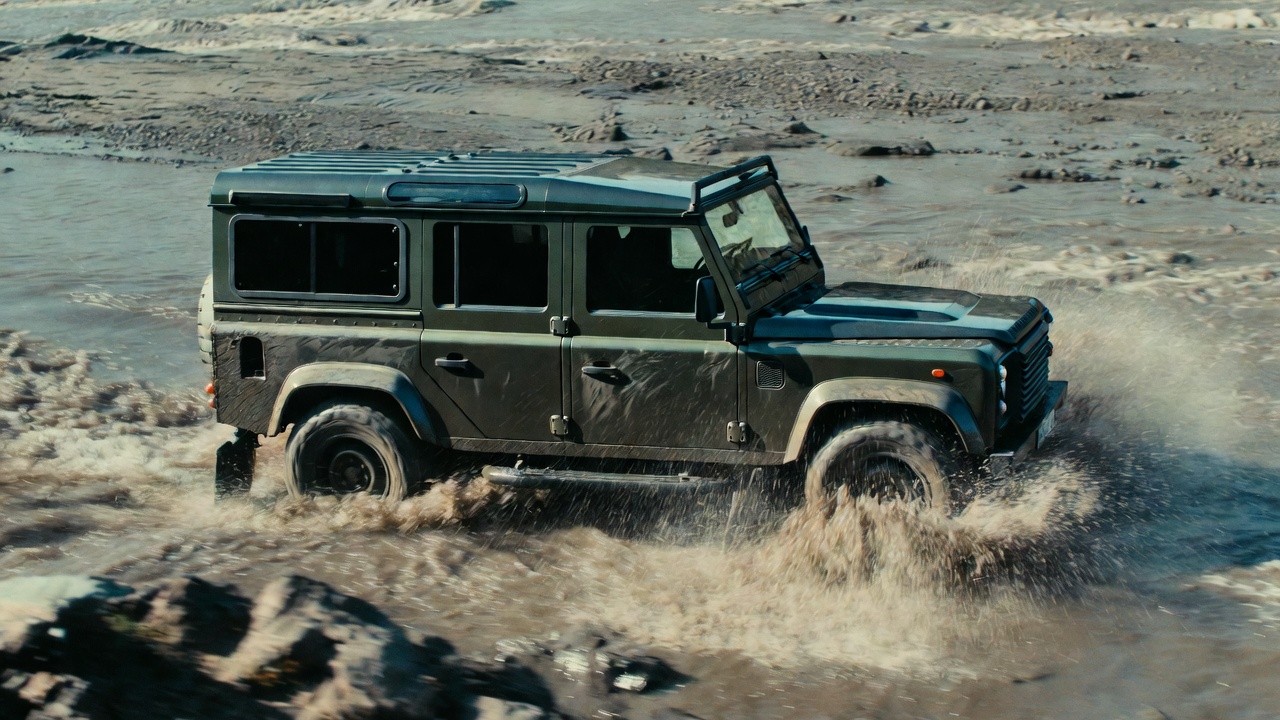 Land Rover Defender 110 wading through river demonstrating off-road capability.