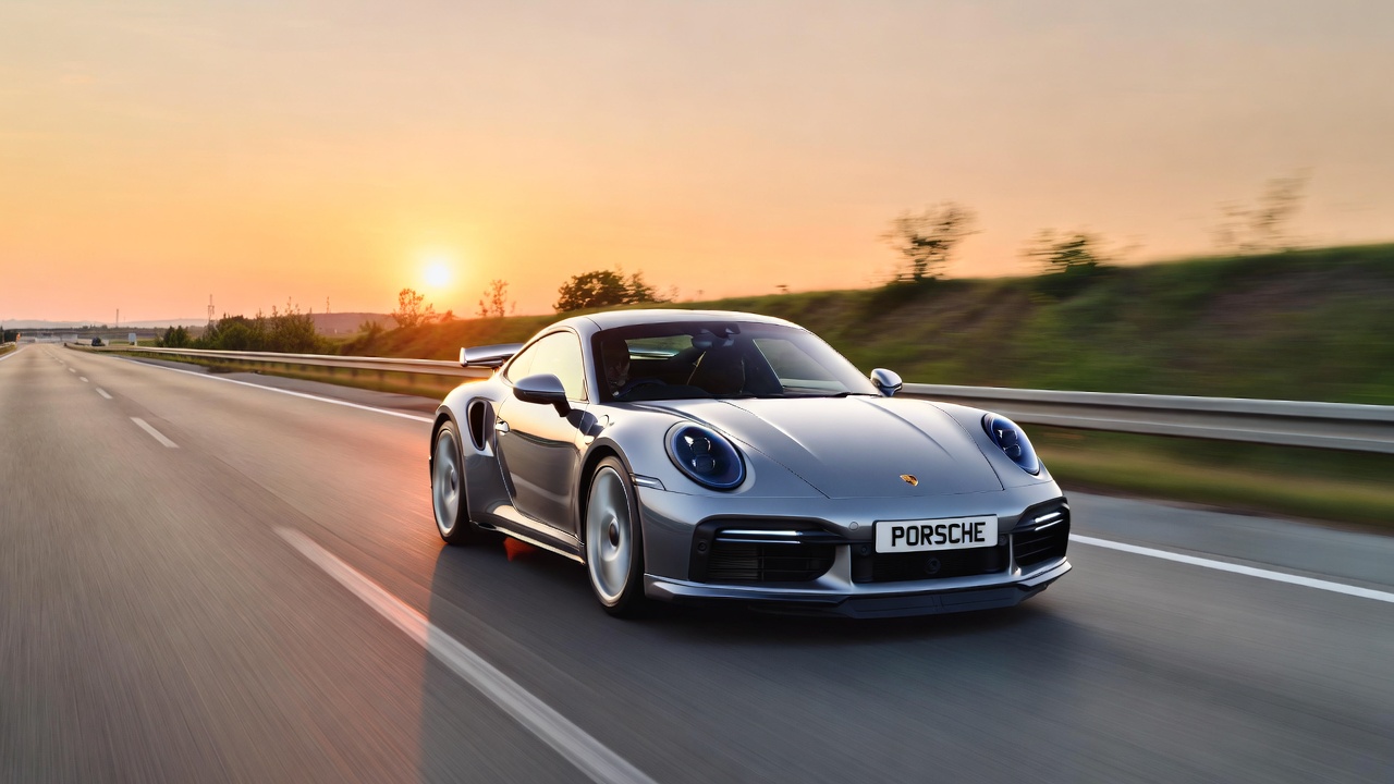 Porsche 911 Turbo S 992 driving at high speed on autobahn during sunrise showcasing supercar performance and stability.