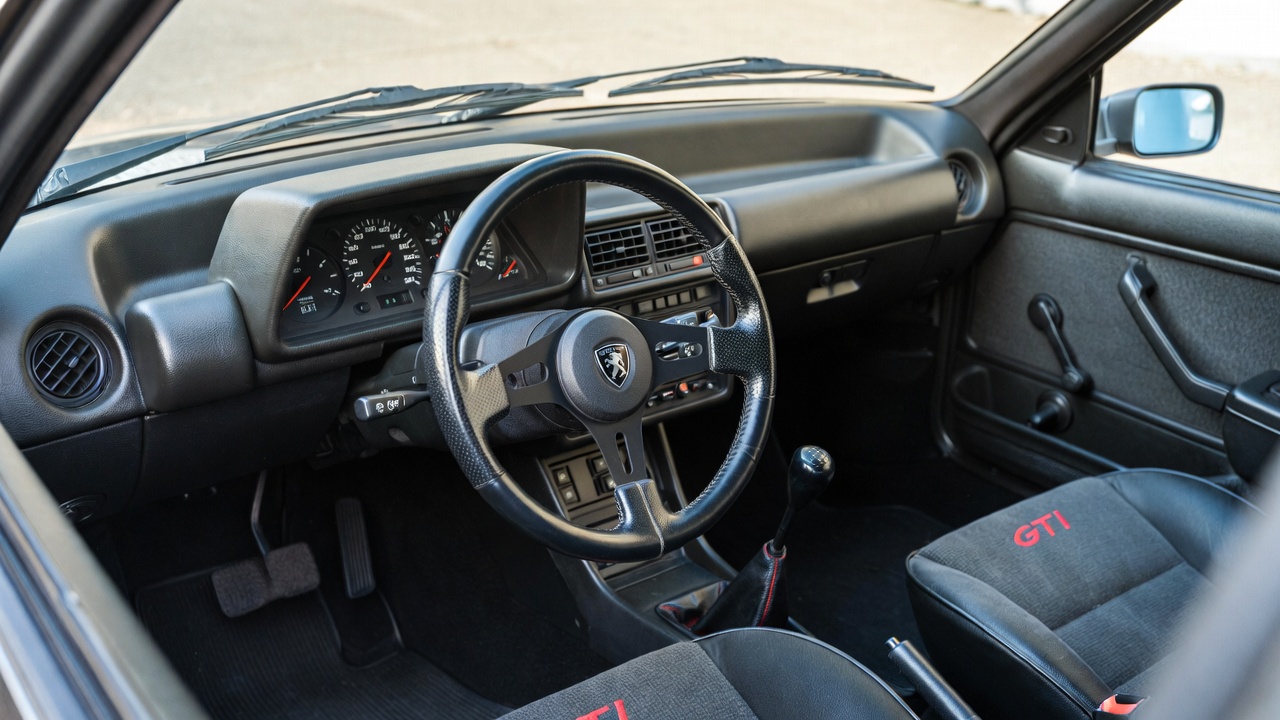 Peugeot 205 GTI interior featuring driver-focused dashboard, analog gauges, and sporty seating.